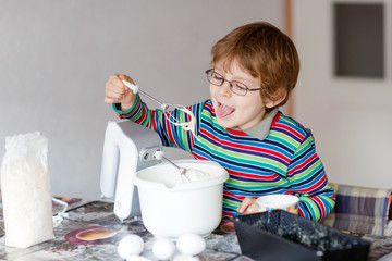 Funny blond kid boy baking cake indoors