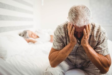 Frustrated senior man sitting on bed