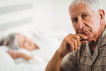 Portrait of worried senior man sitting on bed