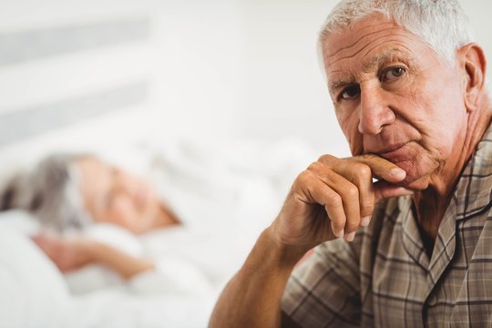 Portrait Of Worried Senior Man Sitting On Bed