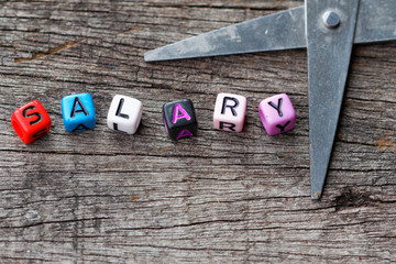 Word salary on colourful cubes and scissor with wooden background. Salary cut concept.
