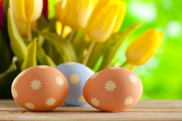 Three Easter eggs on wooden table and fresh tulips