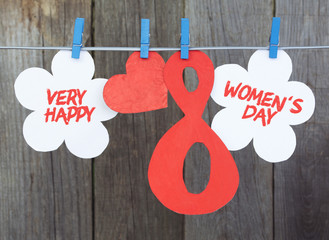 figure 8, paper flowers hang on clothespins in front wooden background. International Women's Day. March 8, Happy Women's Day greeting message text