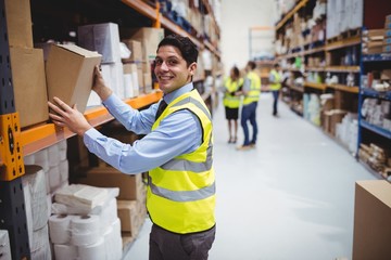 Smiling warehouse worker taking package in the shelf