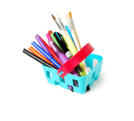 Color pencils, felt-tip pens, brushesin a blue toy basket isolated on  white background. School shopping theme.