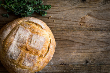 Round bread loaf and bunch of oregano springs on textured wooden background. Table top view. Food background. Copy space for text