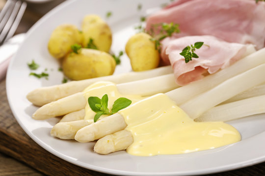 Gekochter Spargel mit Schinken und Kartoffeln auf wei&szlig;em Teller angerichtet
