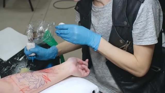 Young female artist tattooing a flower picture on arm of client over a marker pen drawing