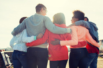 group of happy teenage friends hugging on street