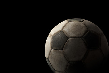 Fototapeta na wymiar Old Soccer Ball on Black Background / Detail of a old black and white soccer ball on a black background with dark shadows