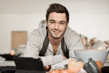 Portrait of a handsome young man cooking with digital tablet in