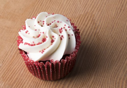 Close up image of a red velvet cupcake with a red wrapper on a wooden board.