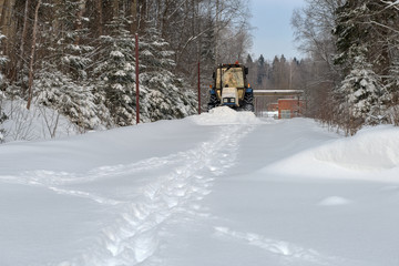 Naklejka premium Tractor in the park clean snow-covered road