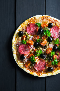 Pizza with salami, olives and herbs
