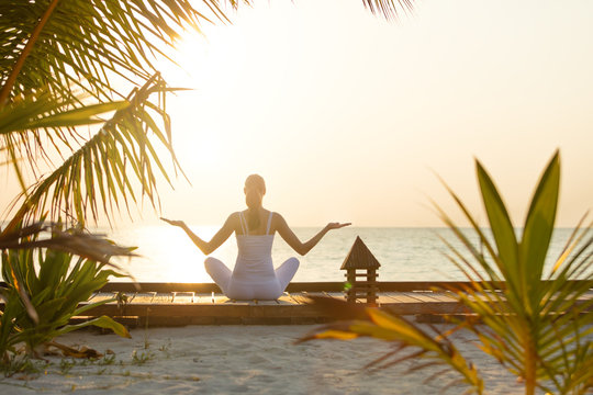 Young woman practicing yoga on the beach at sunset