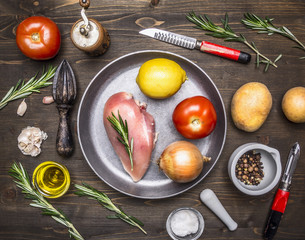 chicken breast, tomatoes, lemon, onion, on pan rosemary, butter, potatoes, ingredients for cooking on wooden rustic background top view close up