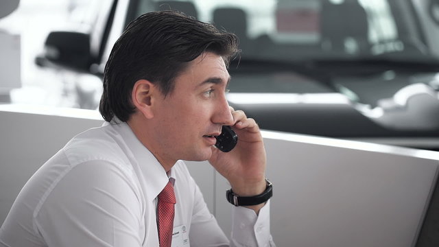 handsome car salesman talking on cell phone in showroom