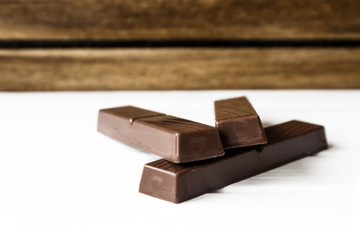 Three chocolate bars on  white base and wooden background 