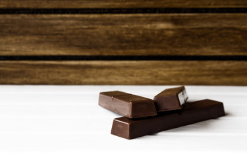 Three chocolate bars on white base and wooden background 