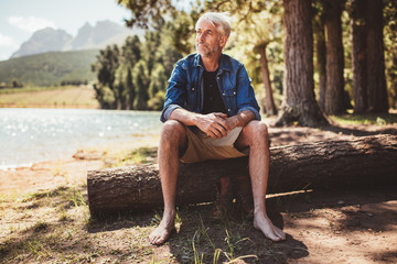 Senior man sitting on a log near lake
