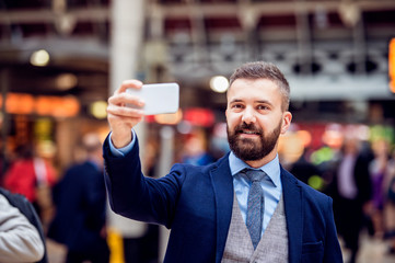 Hipster businessman with smartphone taking selfie, crowded train