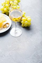 Glass of white wine and assorted cheese with grape on a slate background Copy space