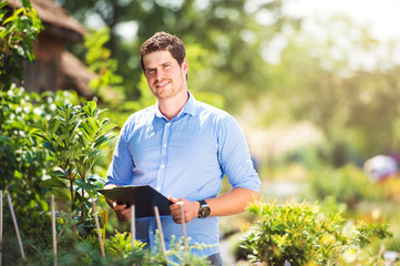 Gardener holding clipboard, in his garden, green sunny nature