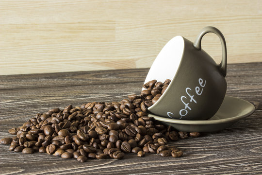 Fototapeta fallen cup with coffee beans and coffee inscription on the wooden table in the background