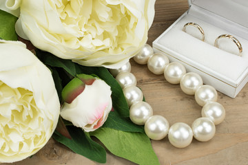 Wedding concept: Golden Wedding Rings, Pearl necklace and Peony flowers on wooden background.