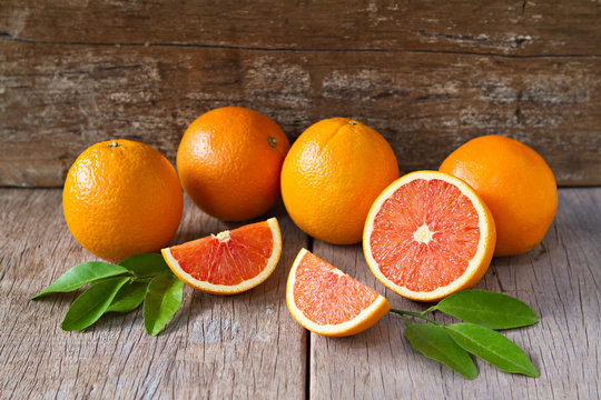 Fresh oranges with slices and leaves on wooden background.