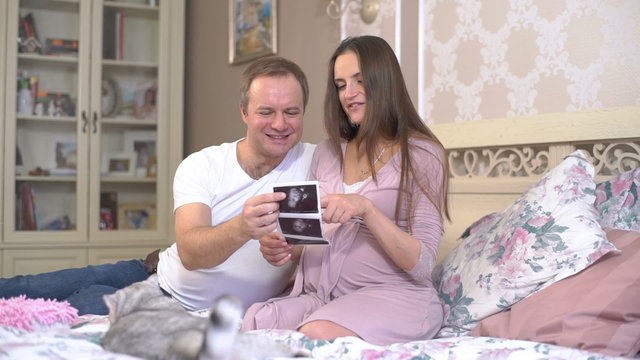 Young pregnant woman and her husband consider photo 3D ultrasound Baby in the womb. Slow motion