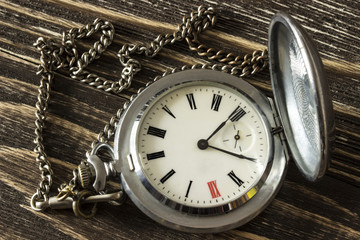 Old silver pocket watch lying on a wooden table. Top view