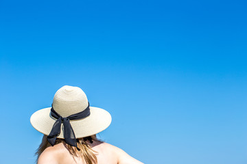 Frau am Strand mit Sonnenhut vor klaren blauen Himmel