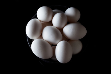 White eggs in a black bowl on black background from above