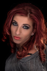 Glamour portrait of fashionable young woman with wavy long red hair and flawless makeup shot against black background