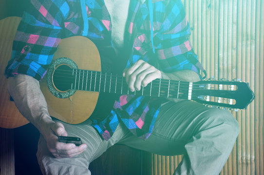 Close Up Of Human Hipster Strong Hands Holding Phone And Old Guitar