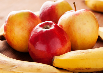 Four ripe red apples and bananas on a wooden table