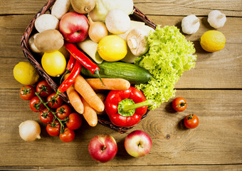 Wicker basket with fruits and vegetables on wooden table