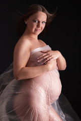 Pretty pregnant woman at studio pregnancy shapes portrait dressed windy, sexy transarent plastic...