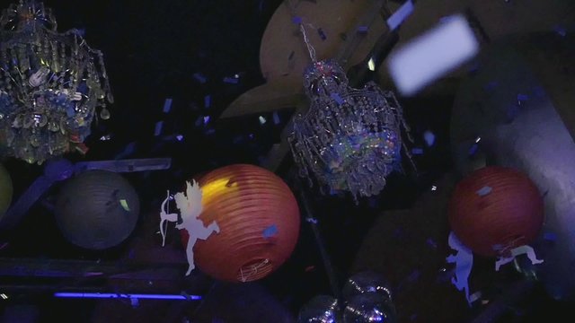 Chandeliers, balls, figures of Cupid hang in nightclub. Confetti. Slow motion