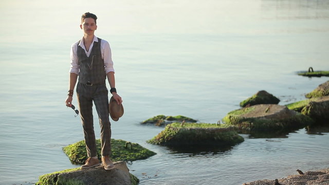 young man in suit and hat standing on a rock