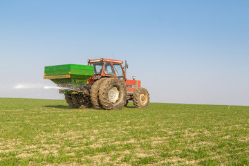 Obraz premium Farmer in tractor fertilizing wheat field at spring with npk