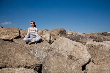 Young attractive woman meditating on the rocks against the sky