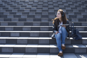 Young woman listening to music on a tablet sitting on the stairs