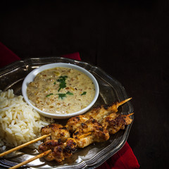 Asian satay chicken skewers with rice and peanut sauce on a silv