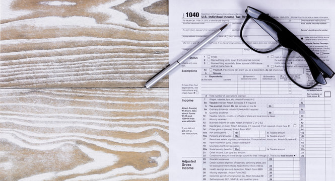 Faded white desktop with tax form and pen with reading glasses