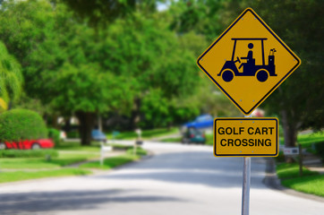 Golf Cart Crossing sign on a residential street intersection with blurred lush green trees in the background
