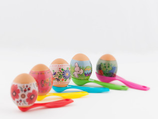 Ornate easter eggs placed on colorful measuring spoons with selective focus on whtie background