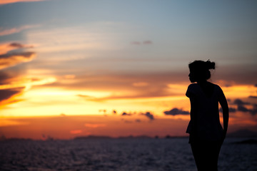 Fototapeta premium The silhouette girl on a cliff above the sea and watching the sunset