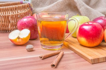 Hot apple drink cider and apples with cinnamon on table.